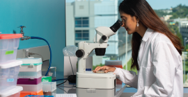 A woman in a white lab coat looks through a microscope.